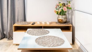 Una habitación moderna con una consola de madera, un sofá blanco con una superficie de cristal, y un florero con flores sobre la consola.