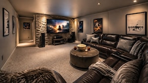 A home theater room with a large flat-screen TV, leather couches, a stone accent wall, and framed artwork.