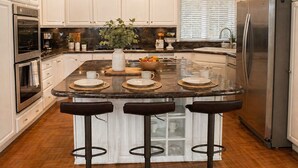 A kitchen with white cabinets, a central island with stools, stainless steel appliances, and a decorative sign.