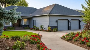 A residential house with a grey exterior, a front yard with red flowers, and a driveway leading to a garage.