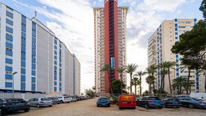 A multi-story building with a central red tower, surrounded by other buildings, parked cars, and palm trees. - Apartment 'Las Damas 10' with Sea View, Wi-Fi and Air Conditioning (Benidorm)