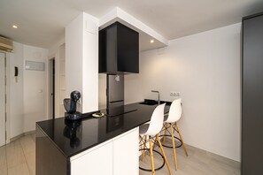 A modern kitchen with a black countertop, white cabinets, a black range hood, and two white chairs.