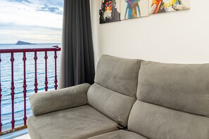 A beige sofa in a room with a view of the sea through a balcony railing.