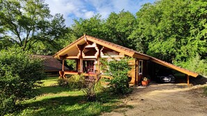 A wooden cabin with a sloped roof, surrounded by lush greenery and trees. - Chalet Le Roy in Mauroux – Relaxation, Nature & Family Fun! (Mauroux)