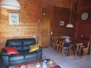 Un intérieur en bois avec un canapé noir, une table à manger et des chaises, ainsi qu’une horloge murale.