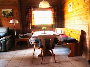 Interior acolhedor de uma cabana com uma mesa de jantar, cadeiras, um sofá, um abajur e cortinas xadrez.
