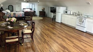 A spacious living area with a wooden floor, a dining table with chairs, a kitchen with white cabinets, and a television. - Light-Filled Loft in 1905 Belhaven Historic Home (Jackson)