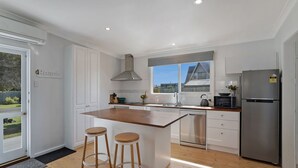 Une cuisine moderne avec des meubles blancs, un îlot central doté de tabourets, un réfrigérateur en acier inoxydable et une fenêtre donnant sur une maison.