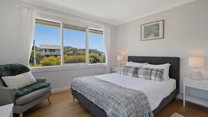 Une chambre à coucher comprenant un lit, deux tables de chevet, une chaise et une fenêtre donnant sur des bâtiments et de la verdure.