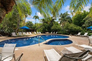 Uma área de piscina com espreguiçadeiras e guarda-sóis, cercada por palmeiras e vegetação.
