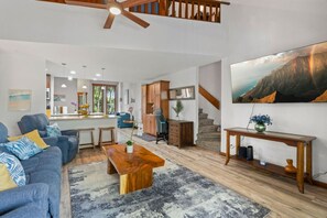 A spacious living area with a sofa, coffee table, and a large painting of a mountain landscape. - Tropical Treehouse Near the Beach (Koloa)