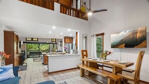 A spacious living area with a dining table, wooden furniture, and a kitchen in the background. - Tropical Treehouse Near the Beach (Koloa)