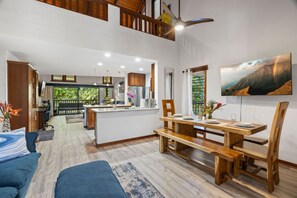 Uma sala de estar ampla com uma mesa de jantar, móveis de madeira e uma cozinha ao fundo.