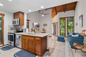 Cozinha moderna com eletrodomésticos de aço inoxidável, armários de madeira e uma ilha grande. Há uma área de refeições com um sofá azul e uma mesa de centro.
