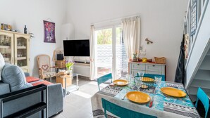 A dining area with a table set for two, a sofa, a TV, and a cabinet with glass doors. - Bastidon at the foot of Ventoux with shared swimming pools and Wi-Fi (Aubignan)