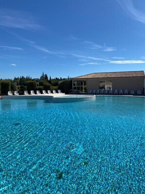 Piscina azul límpida com espreguiçadeiras e um edifício com telhado telhado.
