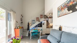 A spacious living area with a grey sofa, a dining table with chairs, a kitchen area, and a staircase leading to another level. - Bastidon at the foot of Ventoux with shared swimming pools and Wi-Fi (Aubignan)