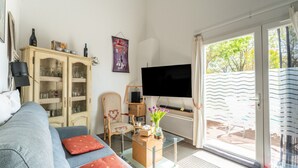 A living room with a sofa, a glass coffee table, a cabinet, a television, and a sliding glass door leading to an outdoor area. - Bastidon at the foot of Ventoux with shared swimming pools and Wi-Fi (Aubignan)
