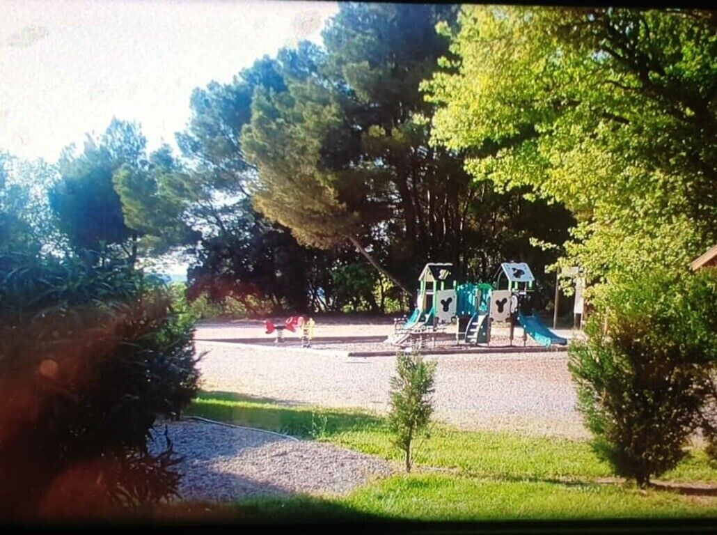 A playground with slides and climbing structures, surrounded by trees and a gravel area.