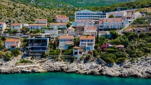 A coastal town with terraced houses, a rocky shoreline, and a mountain in the background. - Spacious 5 bedroom Villa K with sea access  (Zaton)