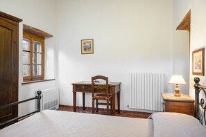 Un dormitorio con una cama, un escritorio de madera, una silla, un radiador y una lámpara.
