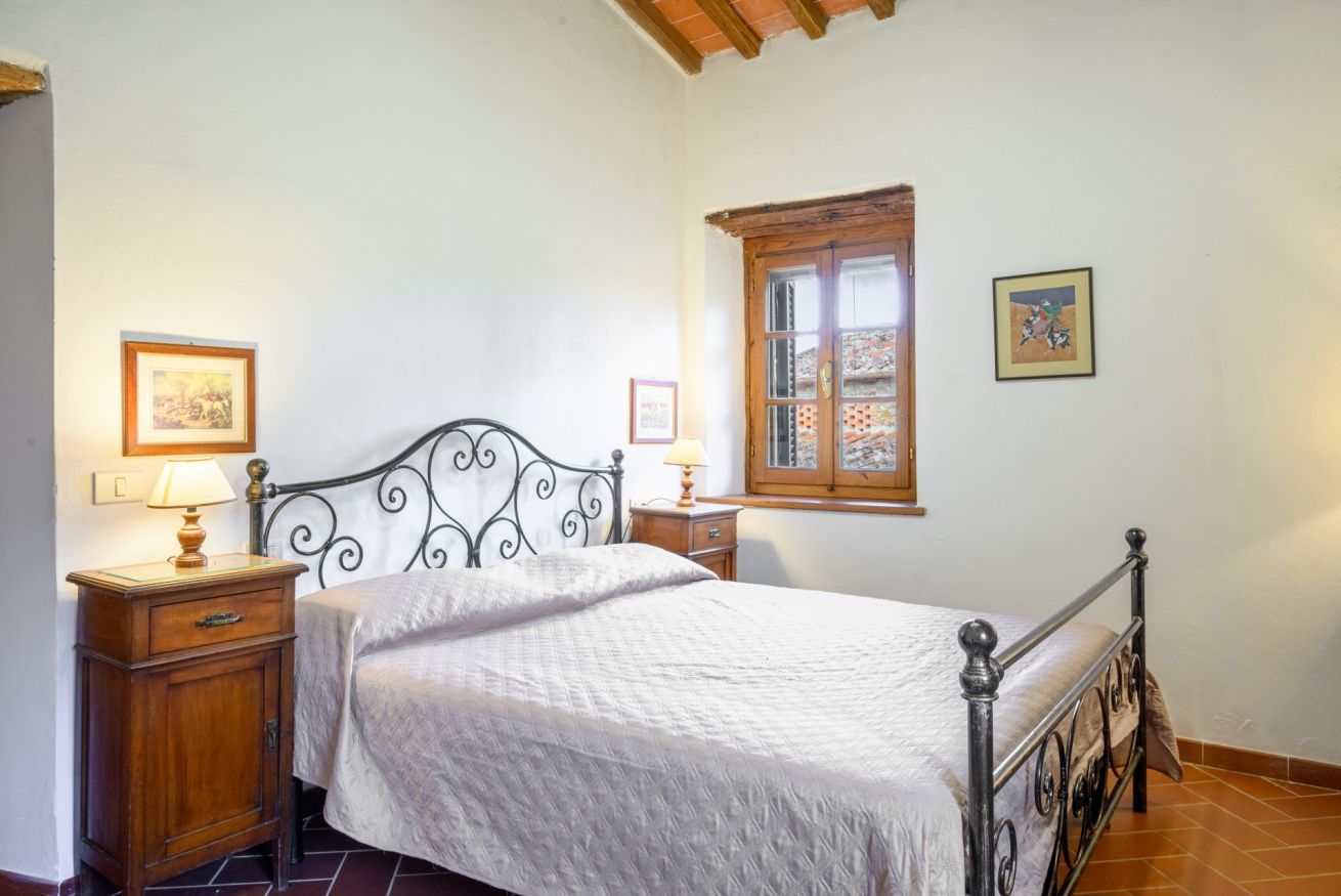 A bedroom with a bed, two bedside tables, a window, and two wall-mounted pictures.