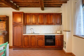 Une cuisine avec des meubles de rangement en bois, un évier, une cuisinière et une fenêtre avec un rideau.