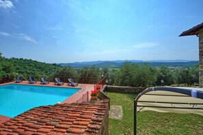 Una piscina con sillones de descanso, un área de estar cubierta y vistas a colinas verdes.