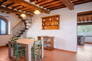Un comedor con una mesa y sillas de madera, una escalera con barandas negras y un estante con objetos decorativos.