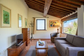 A living room with a TV, sofa, and a window with a view. - Villa Quercina by MMega (Pergine Valdarno)