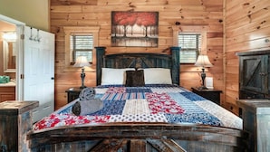 Een slaapkamer in een houten chalet, met een bed, twee bedlampjes, een schilderij boven het bed en een houten garderobe.