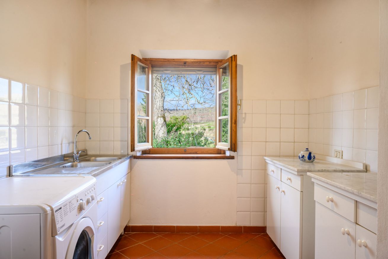 A compact kitchen with a washing machine, a sink, and a window with a view of greenery.