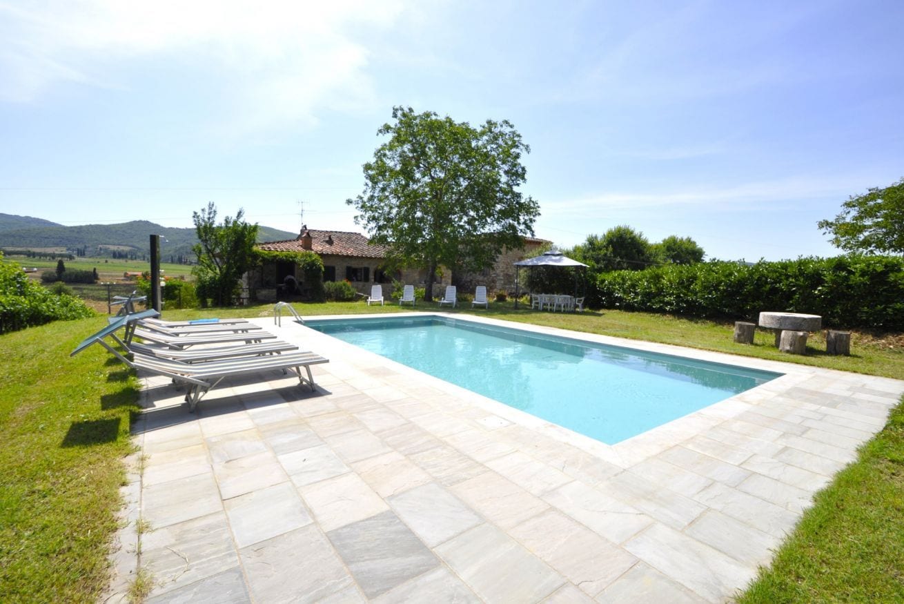 A rectangular swimming pool with a tiled deck, surrounded by a grassy area with a gazebo and lounge chairs.