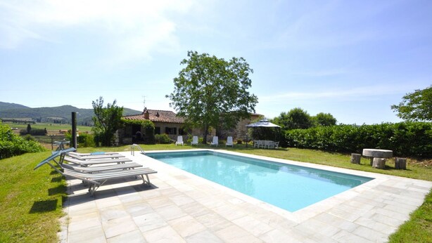 Una piscina rettangolare con bordo piastrellato, circondata da un prato con un gazebo e poltrone relax.