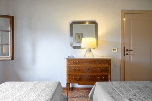 Quarto com duas camas, cômoda de madeira, luminária, espelho e uma porta.