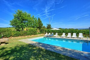 A swimming pool with lounge chairs, surrounded by greenery and trees.