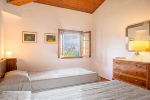 A bedroom with two beds, a wooden dresser, a window with a view, and two framed pictures on the wall.