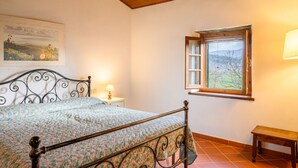 Camera da letto con un letto, un comodino, una lampada, una finestra con persiana aperta e una panca di legno.
