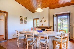Un comedor con una mesa y sillas de madera, una lámpara colgante y una chimenea.