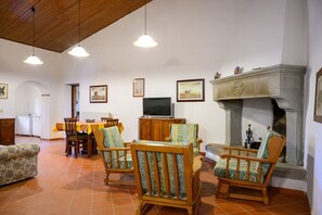 Una sala de estar con chimenea, sillas de madera, un televisor y un comedor con mesa y sillas.