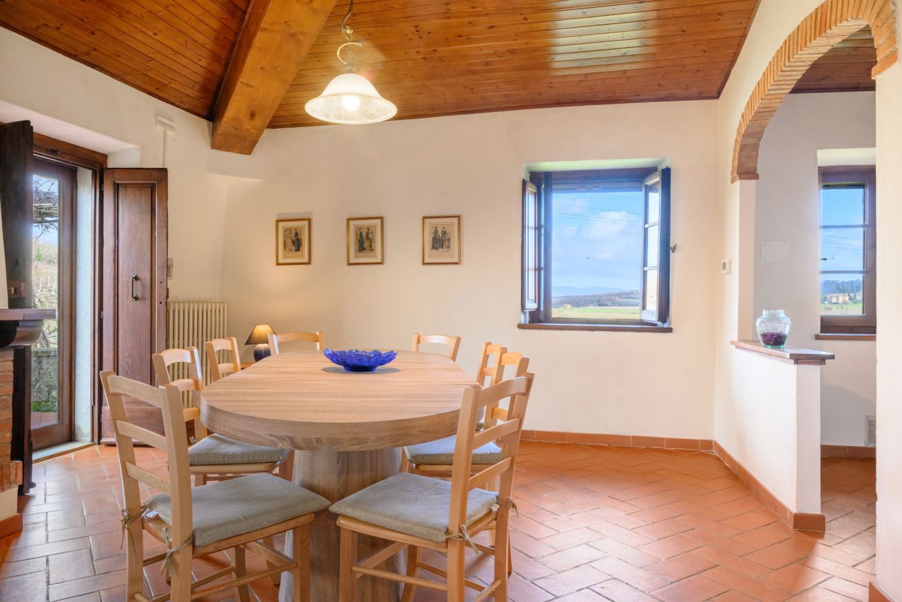A dining area with a round wooden table, chairs, a blue bowl, and framed pictures on the wall.