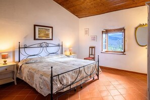 A bedroom with a bed, a nightstand, a chair, a window, and a mirror.