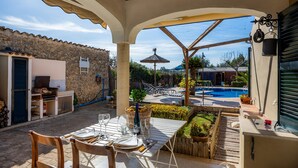 An outdoor patio with a table set for dining, a stone wall, a pool, and a covered area with a thatched roof. - Country House 'Son Macia' with Mountain View, Wi-Fi and Air Conditioning (Selva)