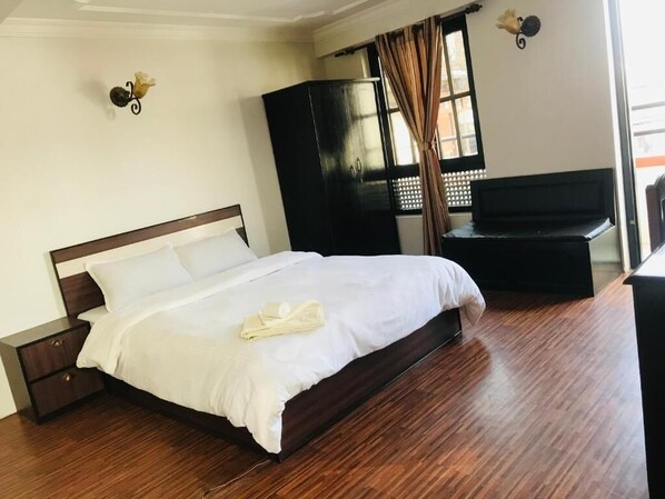 A hotel room with a wooden floor, a bed with white bedding, a wardrobe, and a desk. - Hotel Little Buddha Inn (Kathmandu)