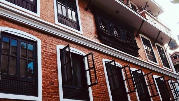 Un edificio de varios pisos con fachada de ladrillo, múltiples ventanas con persianas negras y un balcón en el piso superior.