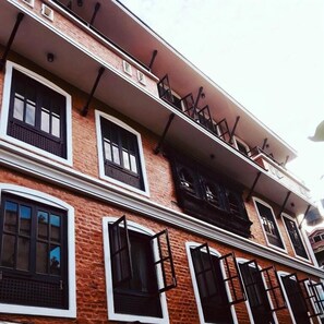 A multi-story building with a brick facade, multiple windows with black shutters, and a balcony on the upper floor. - Hotel Little Buddha Inn (Kathmandu)