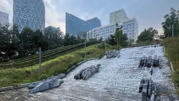 A modern urban landscape with a prominent glass building and a series of water features.