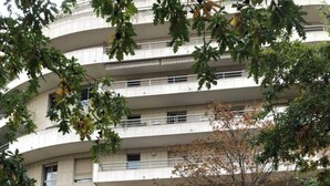 A multi-story building with a modern architectural design, featuring a central entrance with glass doors and a series of balconies on each floor.
