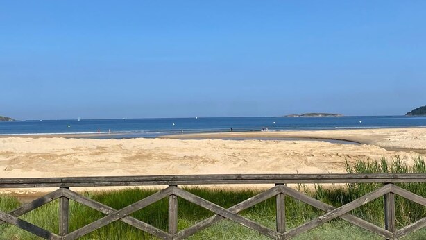 Een strand met een houten omheining op de voorgrond en een helderblauwe lucht.