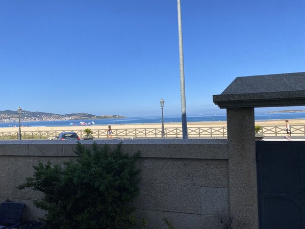 Een kustgezicht met heldere lucht, een strand en een boulevard met een hek.